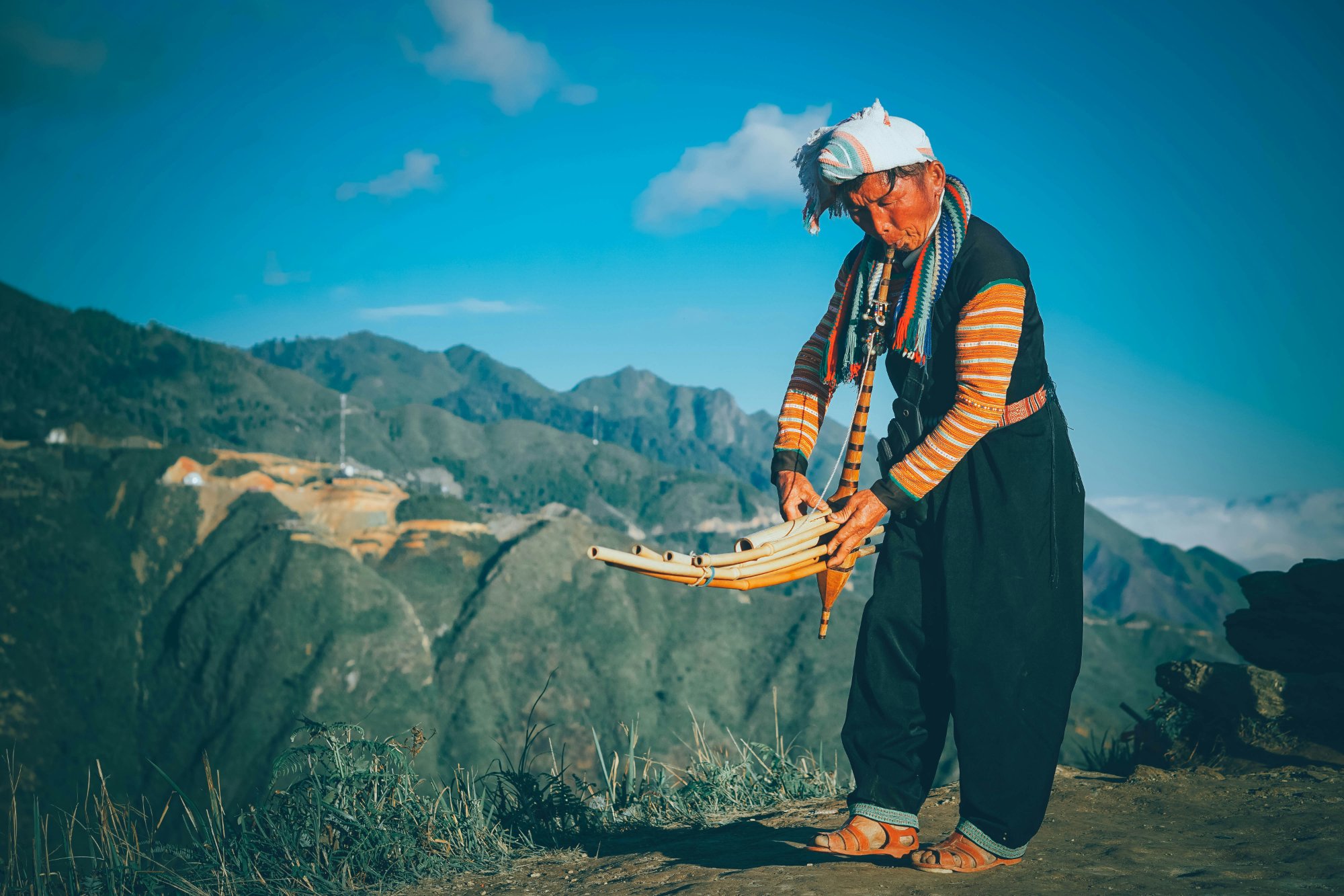 Hmong elder playing traditional instrument in mountain landscape — keeper of soul-calling traditions